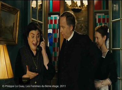   Les Femmes du 6ème étage  de Philippe Le Guay.   Photogramme 21.  M. Joubert attentif aux propos de Dolorès au téléphone. Derrière lui, Maria est-elle heureuse parce qu'elle a entendu l'heureuse nouvelle ou parce qu'une bonne espagnole téléphone de chez un patron ?