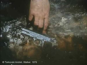 Stalker, Photogramme - 64 : Plan 108.  Gros plan du revolver, la main du Stalker pousse et enfonce le revolver dans l’eau.
