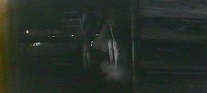 Photogramme  1 : Andreï Roublev, Plan 119. Une femme nue sous un manteau, s'amuse à sauter à travers la fumée d'un petit feu, situé au bas d'un escalier.