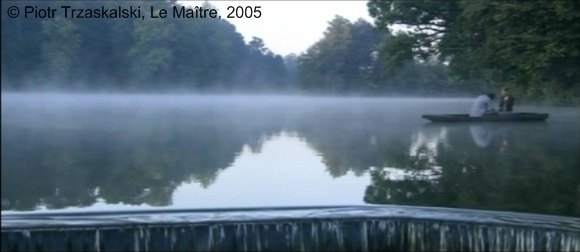 Photogramme : Le Maître, plan 103b. Alexandre et Anna sont dans une barque sur un plan d’eau luxuriant, vaporeux et impressionniste, qui rappelle le monde proustien. Alexandre offre un livre à Anna : Démocrite. Il raconte : Il a imaginé le monde, toi, moi, la barque, l’eau, même ces étoiles, au-dessus, les poissons… Tout ça… C’est ça… Des petites billes. Des atomes. Petites comme ça… La ville, la campagne, même les chiens dans leurs niches sont faits de ces petites billes. Tout est organisé une fois pour toutes, et c’est immuable…Tout… Mais, tu vois, parfois une de ces billes peut se tromper, perdre son chemin, errer, sortir de son orbite…
