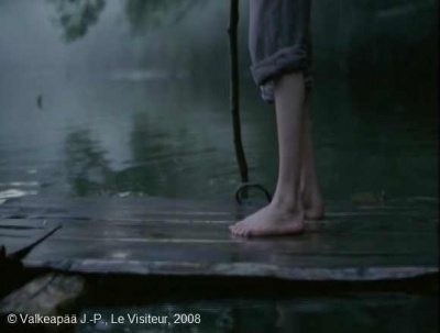 Le Visiteur, (Muukalainen), photogramme - plan 138, l’Enfant monte sur le radeau et grâce à une perche en bois qu'il appuie au fond de l'eau il dirige son embarcation avec précision, tout en restant à l'affût des bruits environnants.