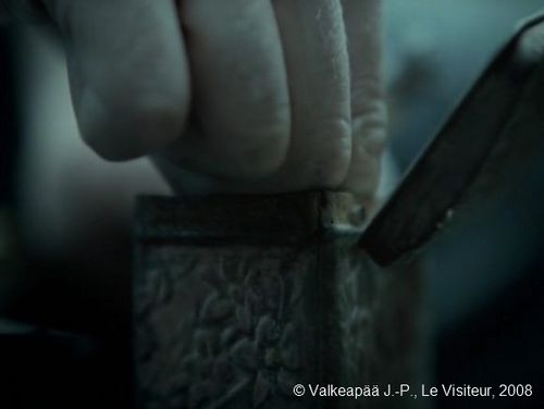 Le Visiteur, plan 165. Le père soulève le petit cache (le double fond), et prends avec deux doigts l’objet mystérieux au fond du coffre. Nous apprenons ainsi, que l’objet mystérieux est de petit taille, comme une perle par exemple.