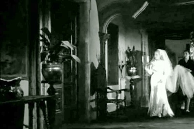  Viridiana de Luis Buñuel.     Photogramme  - Plan 42. Viridiana qui apparaît vêtue de la robe de mariée, elle porte d’une main un chandelier allumé. Elle s’avance, parée comme si elle montait à l’autel. Ramona l’aide en portant sa traîne.