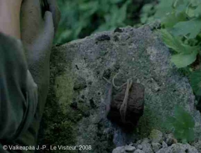 'Le Visiteur, (Muukalainen), photogramme - plan 140, l’Enfant arrive à la destination voulue, il s'agit d'un vieux puits. Il s'assied sur une pierre, il sort le petit coffre (3ème représentation) enroulé, à son tour, d'une fine ficelle, et le dépose à côté de lui.
